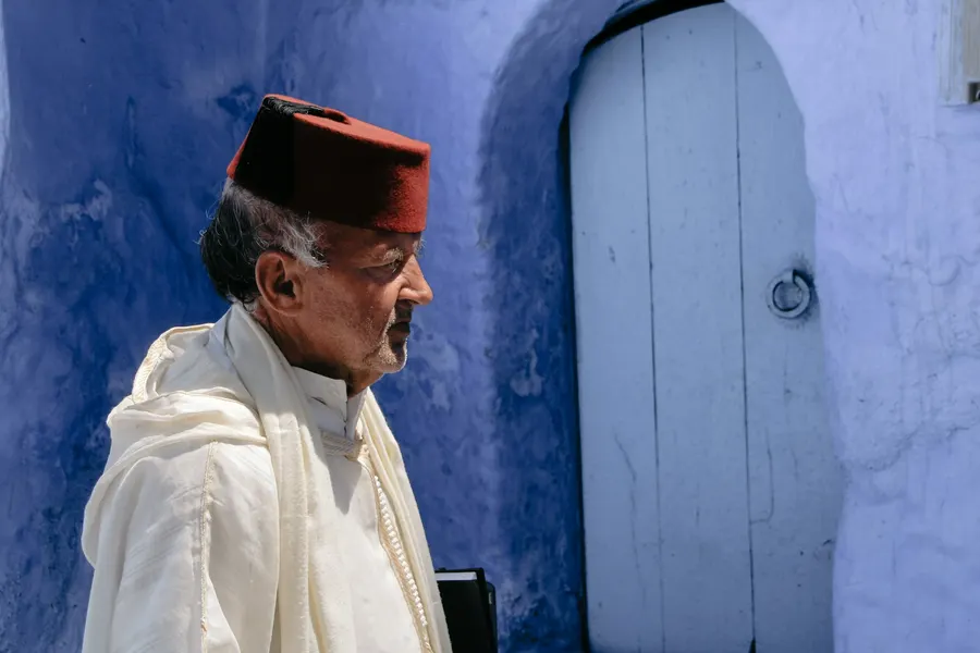Elderly Moroccan man in tarboosh cap by a blue doorway in Chefchaouen