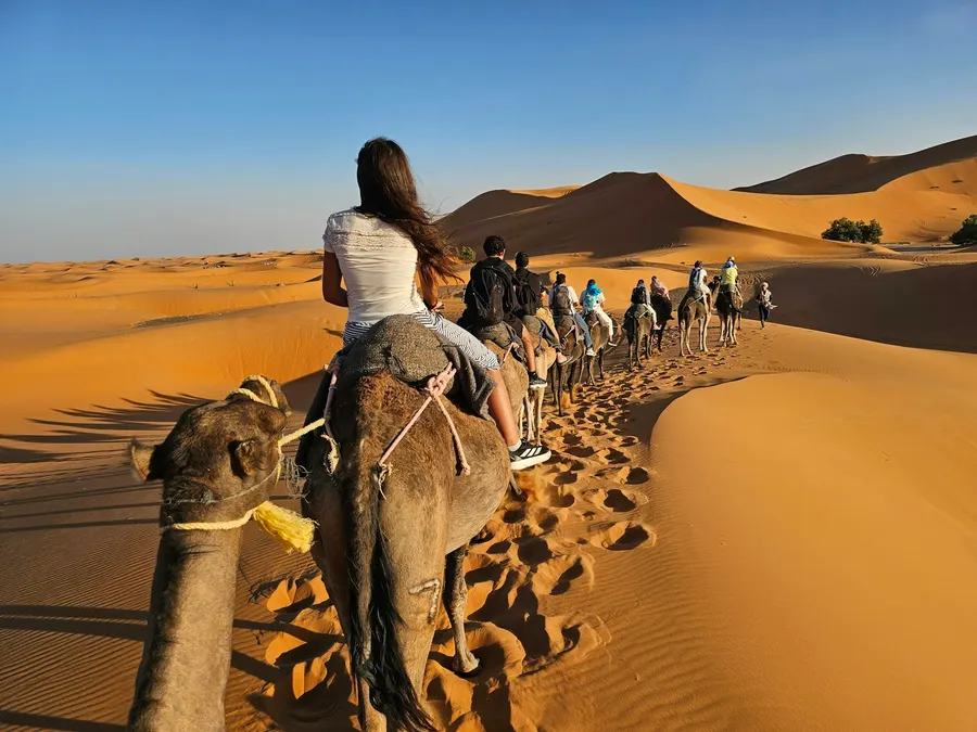 Travelers riding camels across desert sand dunes towards camp