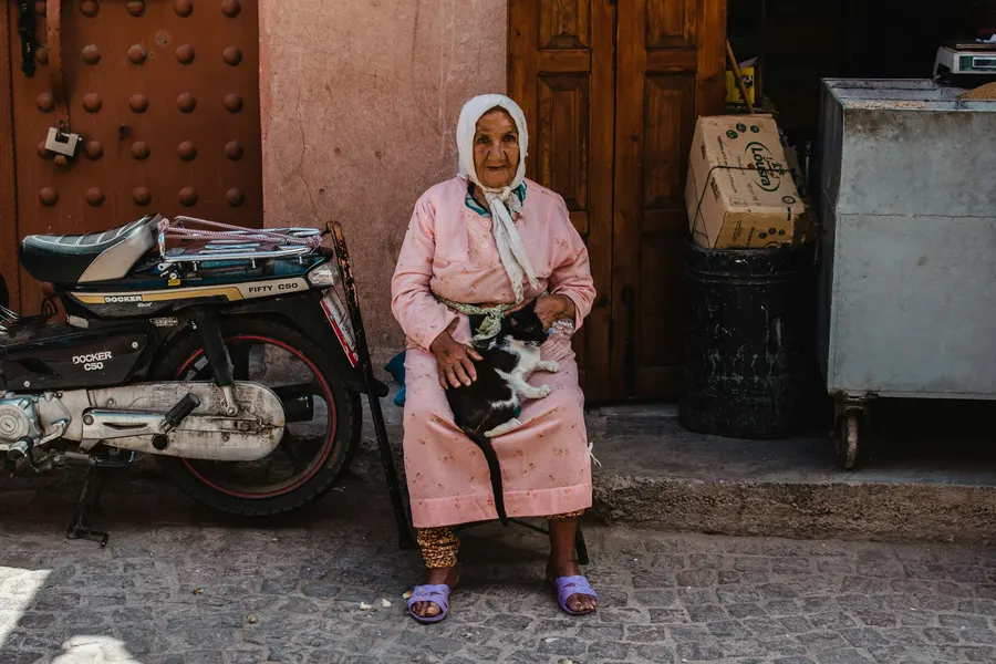 Moroccan woman sitting with a cat outside a medina shop