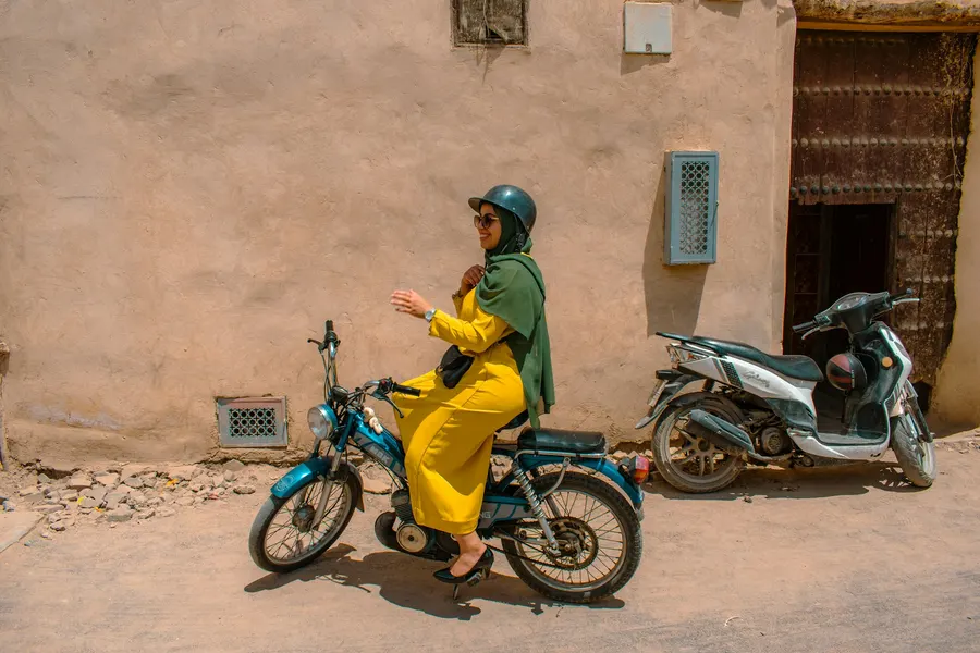 Woman in yellow riding a vintage moped in a Marrakech medina street
