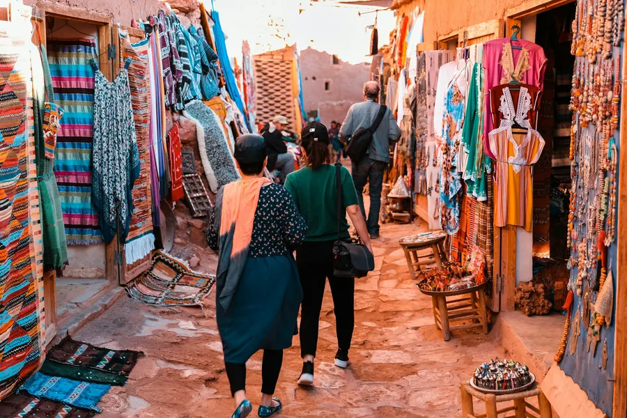 Tourists exploring colorful carpet and handicraft shops in Ait Ben Haddou