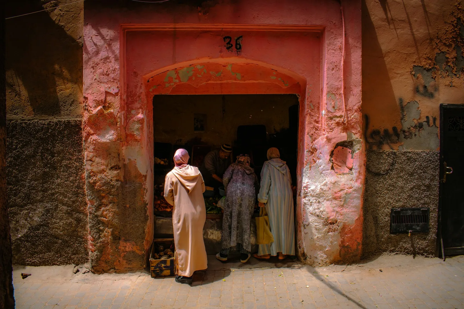 Women in traditional djellabas shopping at a medina produce stall in Marrakech