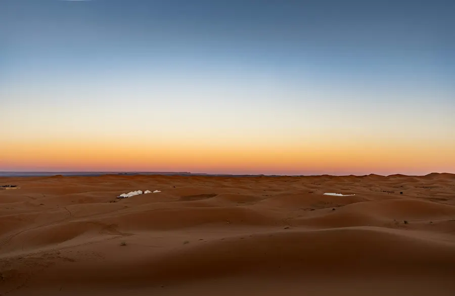 White tents of a luxury desert camp nestled between sand dunes at dusk