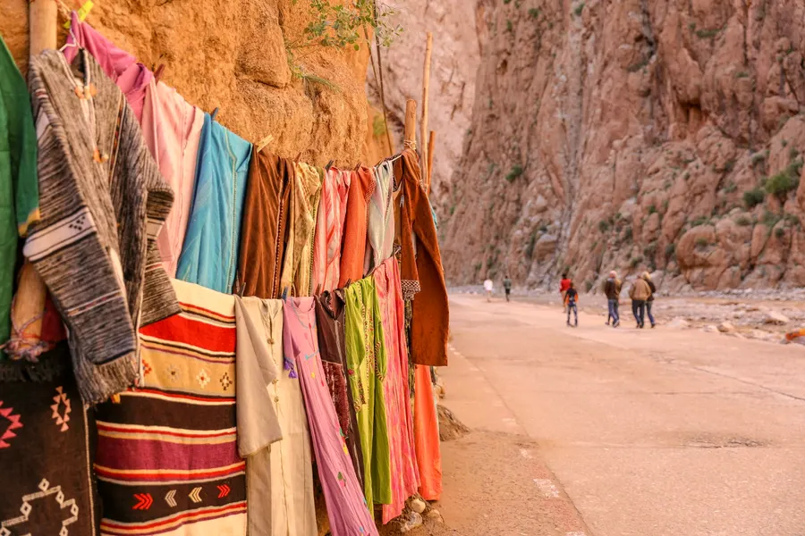 Traditional djellabas and textiles for sale along Todra Gorges canyon wall