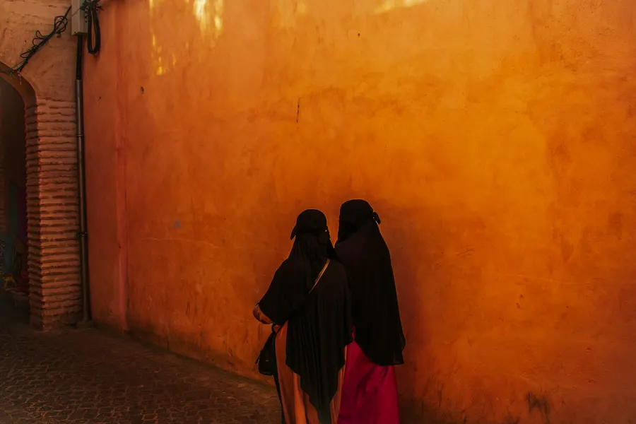 Mujeres tradicionales en abayas caminando por un callejón ocre de la medina