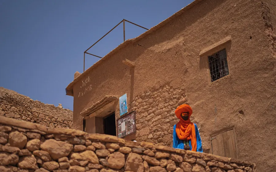 Hombre local con turbante naranja frente a una edificación de adobe en aldea del desierto