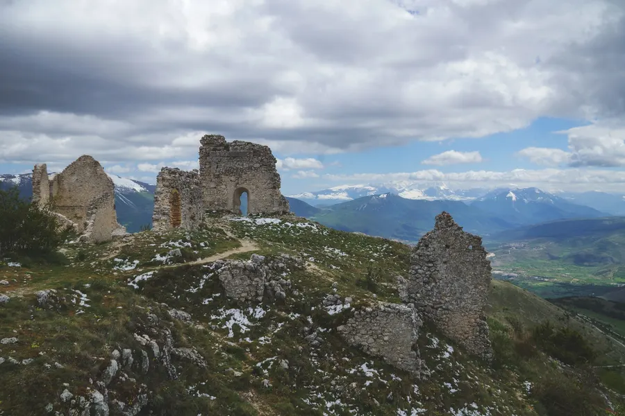 Ruinas de antigua fortaleza de piedra en una cresta montañosa con cumbres nevadas
